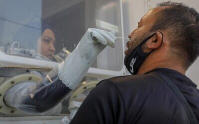 A paramedic from Magen David Adom collects a swab sample from a man at a COVID-19 mobile testing station in East Jerusalem on August 19, 2020. (AHMAD GHARABLI / AFP)