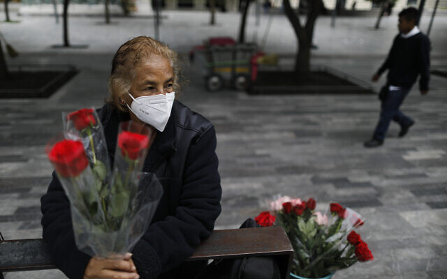 Wearing a mask to curb the spread of the new coronavirus, Martha Gonzalez Reyes, 76, sells roses outside Metro Hidalgo in central Mexico City, Monday, Aug. 10, 2020. After four months staying at home, Gonzalez returned to selling on August 1, but she says business hasn't fully rebounded. "People have less money to spend she says, and they don't want to go out and get infected."(AP Photo/Rebecca Blackwell)