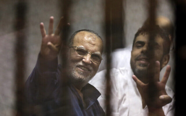Senior Muslim brotherhood leader Essam el-Erian, left, flashes the four-fingered symbol of Rabaah that refers to the deadly dispersal of supporters of former Egyptian President Mohammed Morsi in August 2013, inside a makeshift courtroom at Egypt's National Police Academy, in Cairo, Egypt, on April 21, 2015. (AP Photo/Amr Nabil, File)