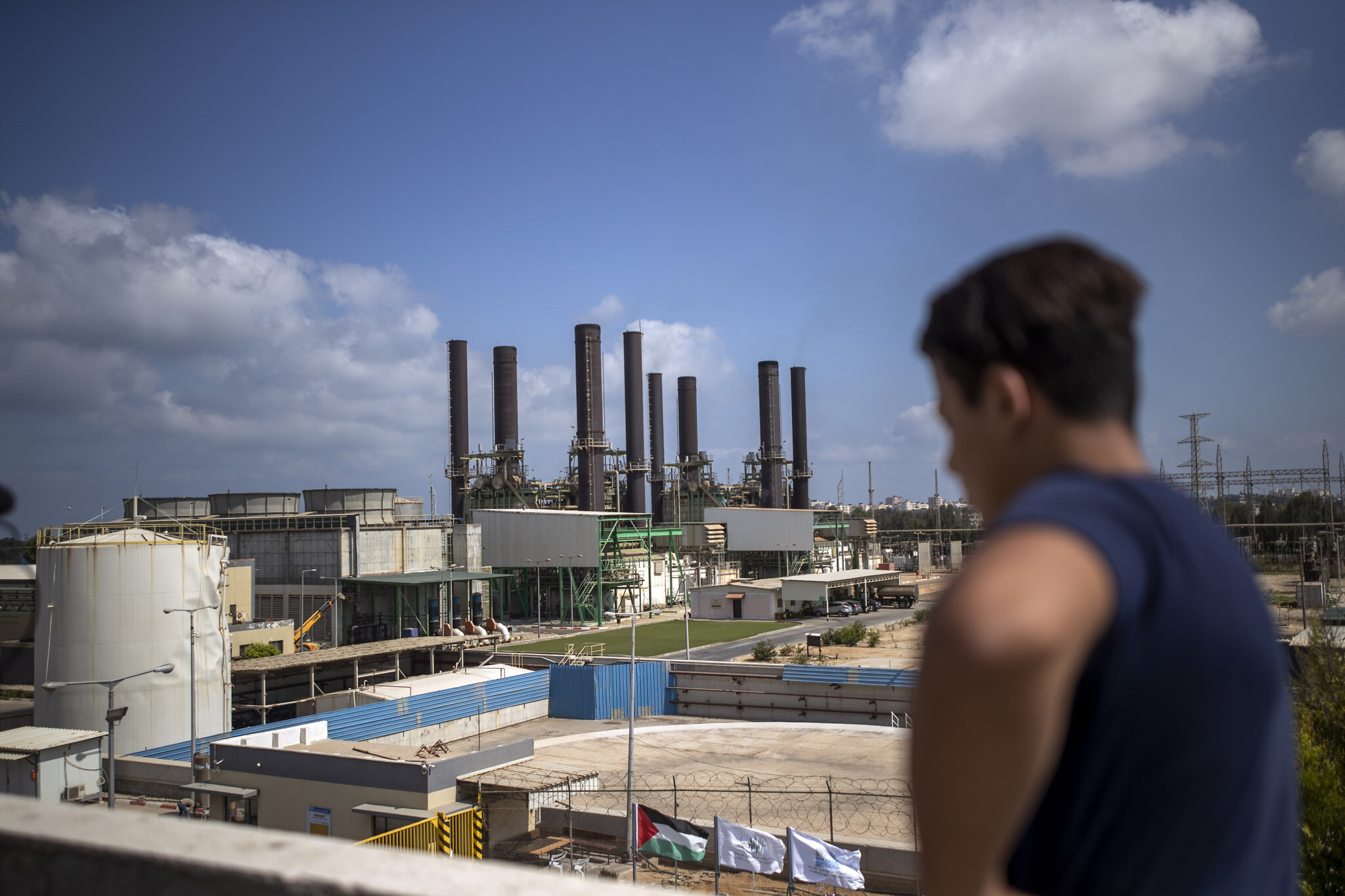A Palestinian man, on the rooftop of his home, looks at Gaza’s power plant after it was shut down, in the town of Nusairat, central Gaza Strip, August 18, 2020. (AP Photo/ Khalil Hamra)