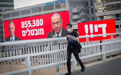 A man wearing a protective mask walks by a sign stating the number of unemployed in Israel, alongside the word 'Enough!!' in Tel Aviv, on July 22, 2020 (Miriam Alster/Flash90)