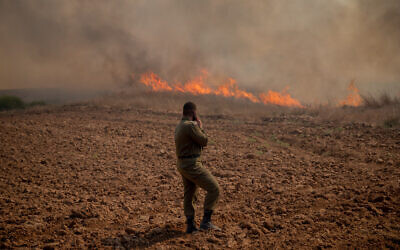Illustrative: An IDF soldier stands in front of a fire near Kibbutz Be’eri in southern Israel that was sparked by a balloon-borne incendiary device launched from the Gaza Strip, August 13, 2020. (Yonatan Sindel/Flash90)