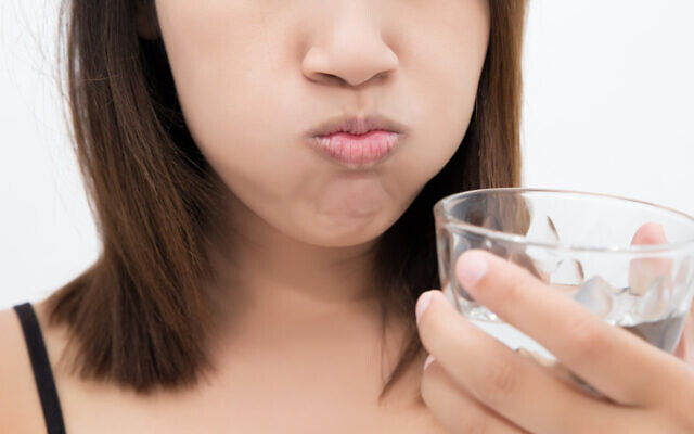 Illustrative: A woman gargles while using mouthwash from a glass (Tharakorn; iStock by Getty Images)