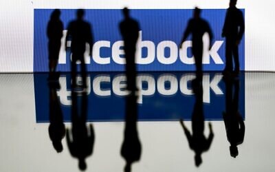 Silhouettes are seen in front of the logo of US social media Facebook in Brussels, February 14, 2020. (Kenzo TRIBOUILLARD / AFP)