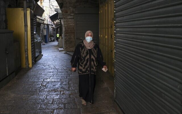 A Palestinian woman wearing a protective mask walks on an empty street lined with closed shops in Jerusalem's Old City, on September 19, 2020, amid a nationwide lockdown due to a spike in coronavirus infections. (Menahem Kahana/AFP)