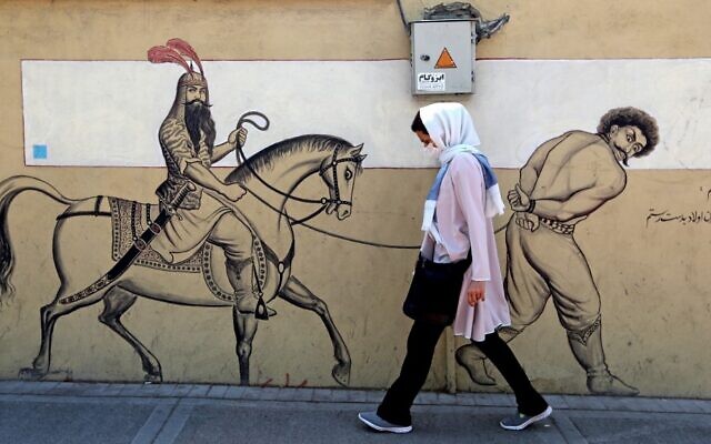 A woman, wearing a protective mask due to the COVID-19 coronavirus pandemic, walks past a graffiti depicting the legendary Persian hero Rustam (or Rostam) riding his horse behind a bound prisoner in Iran's capital Tehran on September 20, 2020. (ATTA KENARE/AFP)