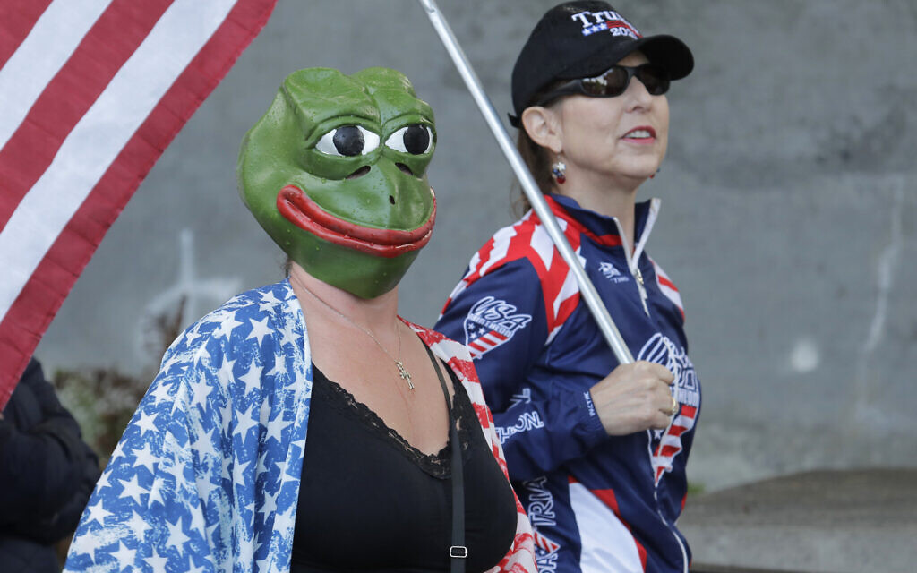 A woman wears a mask of Pepe the Frog, a cartoon figure appropriated by far-right groups, as she stands next to a woman holding a US flag and a "Trump 2020" hat, Thursday, May 14, 2020, during a protest rally at the Capitol in Olympia, Wash.  (AP Photo/Ted S. Warren)