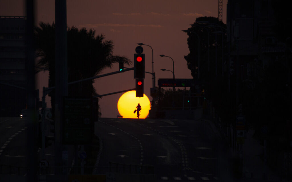 A person rides a bicycle on an empty street as the sun sets on the first day of a three-week lockdown in Tel Aviv, September 18, 2020. (AP Photo/Ariel Schalit)