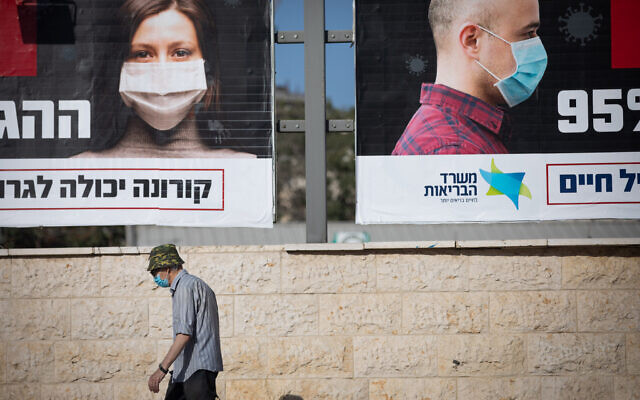 People walk past a billboard posted by the Health Ministry instructing people to wear face masks, in Jerusalem on October 11, 2020. (Yonatan Sindel/Flash90)
