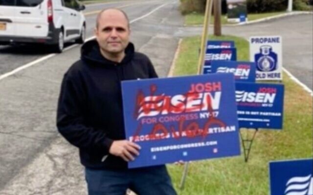 Congressional candidate Josh Eisen holds a campaign sign tagged with anti-Semitic graffiti. (Screenshot from News12 via JTA)