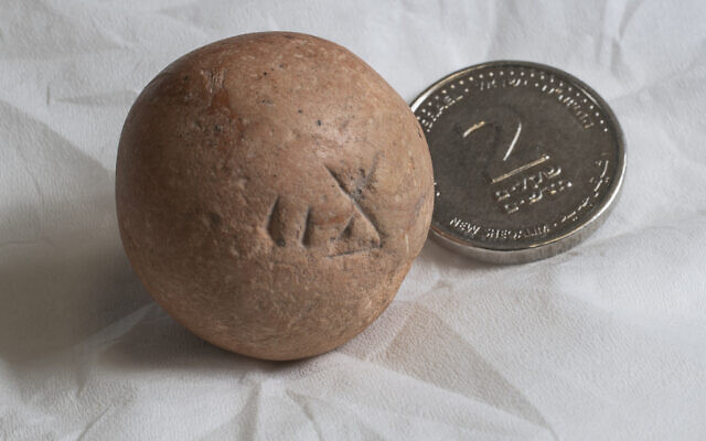 The 2,700-year-old limestone two shekel weight next to a modern two shekel coin. (Shai Halevi, Israel Antiquities Authority)