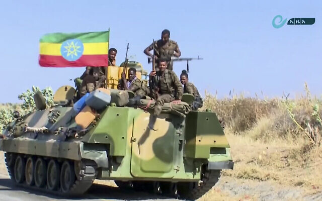 Screen capture from undated video released by the state-owned Ethiopian News Agency on November 16, 2020 shows Ethiopian military personnel sitting on an armored personnel carrier next to a national flag, on a road in an area near the border of the Tigray and Amhara regions of Ethiopia. (Ethiopian News Agency via AP)