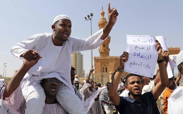A man holds a poster with Arabic that reads, 'We will not give up, we will not sell out, we will not agree on normalization,' as others chant slogans to protest Sudanese President of the Sovereignty Council Abdel Fattah Abdelrahman Burhan's contentious decision to meet Prime Minister Benjamin Netanyahu in a move toward normalizing relations, in Khartoum, Sudan, Feb. 7, 2020. (AP Photo/Marwan Ali)