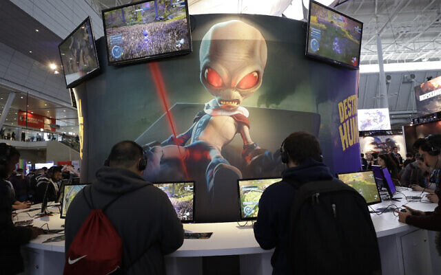 ILLUSTRATIVE -- An image of 'Crypto,' the main character in the video game 'Destroy All Humans!,' appears above people playing video games at the THQ Nordic exhibit, Feb. 27, 2020, at the Pax East conference in Boston. (AP Photo/Steven Senne)