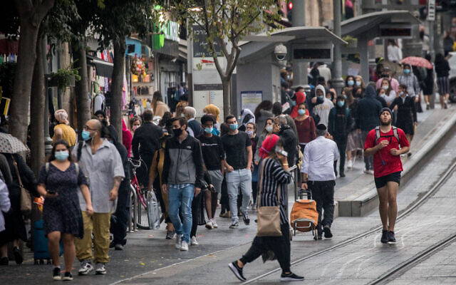 People wearing face masks take cover from the rain on Jaffa Street in downtown Jerusalem, on November 11, 2020. (Yonatan Sindel/Flash90)