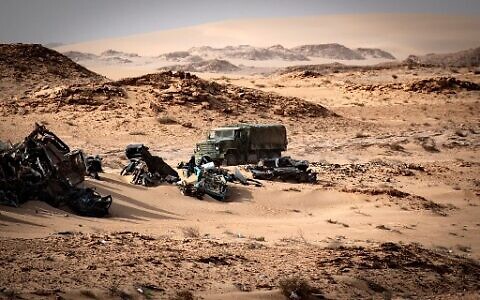 A Moroccan army vehicle drives past car wreckage in Guerguerat located in the Western Sahara on November 24, 2020, after an intervention of the royal Moroccan armed forces in the area. (Fadel Senna/AFP)