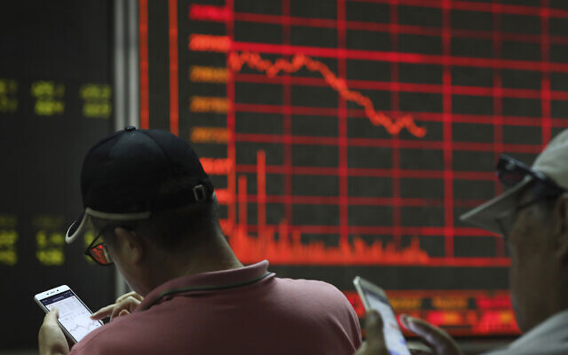Illustrative: Investors check stock prices on their mobile phones near a display of the stock market index at a brokerage in Beijing on Wednesday, June 12, 2019. (AP/Ng Han Guan)