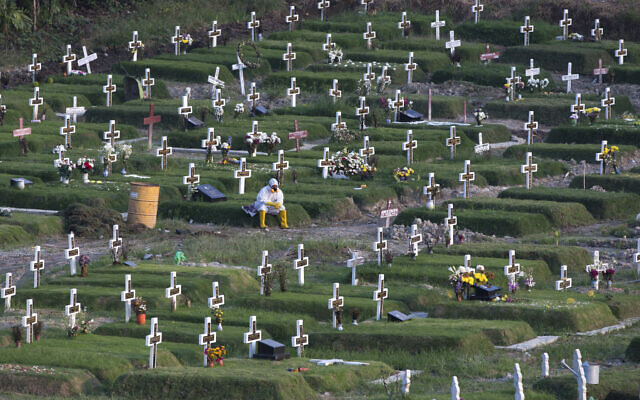 A worker in protective suits takes a break amid graves at a newly opened cemetery for the victims of COVID-19 in Medan, North Sumatra, Indonesia, November 16, 2020. (Binsar Bakkara/AP)