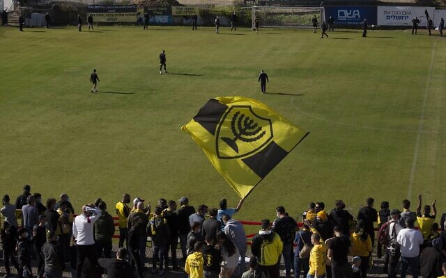 Beitar Jerusalem soccer supporters sing and wave their flag as players enter the pitch during a team training session in Jerusalem, December 11, 2020. (AP Photo/Maya Alleruzzo)