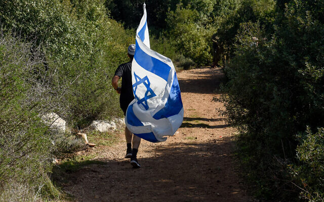 A person runs with an Israeli flag in the Reihan forest near Tal Menashe in the West Bank where Esther Horgen was found dead in suspected terror attack, Dec. 21, 2020. (Flash 90/Meir Vaknin)