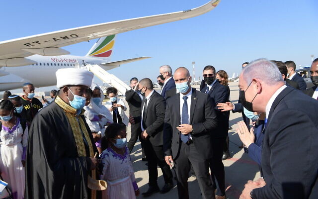 Prime Minister Benjamin Netanyahu, right, greets members of the Ethiopian Jewish community as they arrive at  Ben Gurion airport, outside Tel Aviv, on December 3, 2020. (Amos Ben Gershon/GPO)