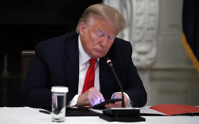 In this June 18, 2020 file photo, US President Donald Trump looks at his phone during a roundtable with governors on the reopening of America's small businesses, in the State Dining Room of the White House  in Washington.  (AP Photo/Alex Brandon, File)
