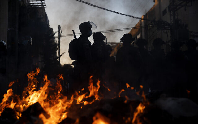 Police officers stand guard next to burning garbage during clashes with ultra-Orthodox Jews in Bnei Brak, Israel, January 24, 2021. (AP Photo/Oded Balilty)