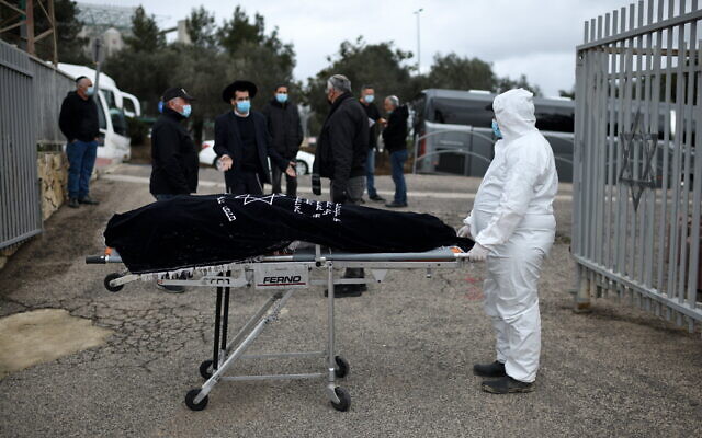 A burial services employee carries the body of Romania-born Holocaust survivor Golda Schwartz, who died at the age of 93 of complications of COVID-19 in Nof Hagalil Cemetery on January 28, 2021 (Gili Yaari / Flash90)