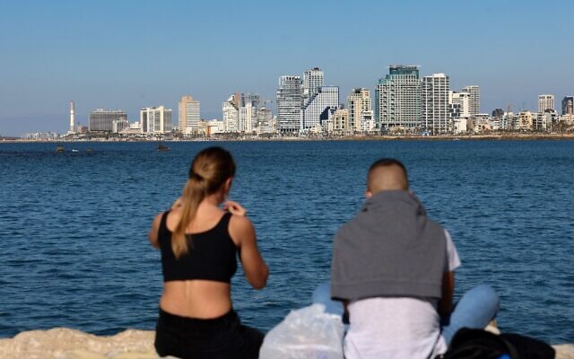 A young couple share a picnic in front of a view of the Tel Aviv skyline, in the Israeli coastal city, on February 15, 2021 (Emmanuel DUNAND / AFP)
