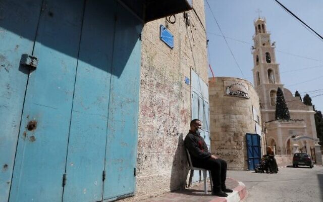 A Palestinian man wearing a protective mask sits outside a closed shop in the West Bank town of Beit Sahur, near Bethlehem amid a tightened lockdown due to the COVID-19 pandemic on February 24, 2021. (Photo by HAZEM BADER / AFP)