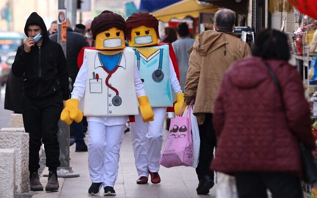 People dressed as Lego medical workers walk past shops in Jerusalem on February 24, 2021, a day before the Jewish holiday of Purim. (Emmanuel Dunand/AFP)