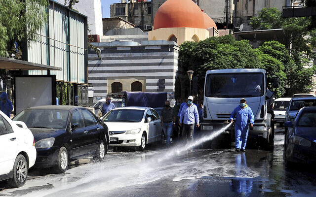 A Syrian worker disinfects a street to prevent the spread of coronavirus in Damascus, Syria, August 3, 2020. (SANA via AP)