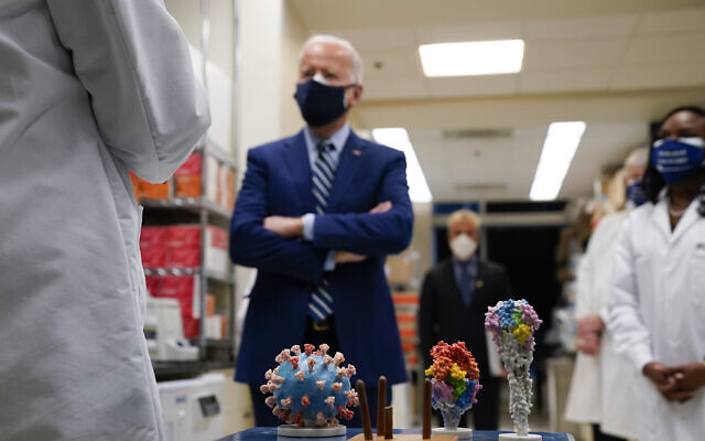 With a model of the COVID-19 virus displayed, US President Joe Biden listens as Dr. Barney Graham, left, speaks during a visit at the Viral Pathogenesis Laboratory at the National Institutes of Health (NIH), on Thursday, February 11, 2021, in Bethesda, MD. (AP Photo/Evan Vucci)