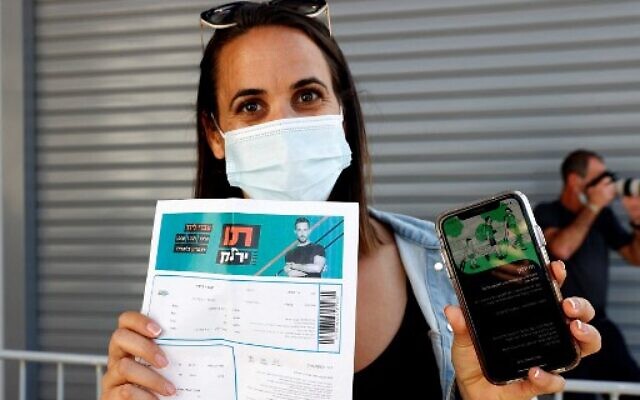 An attendee shows off a "green pass" (proof of being fully vaccinated against COVID-19 coronavirus disease) upon arrival at Bloomfield Stadium in Tel Aviv, on March 5, 2021, before attending a "green pass concert" for the vaccinated, organized by the Tel Aviv municipality. (Jack Guez/AFP)