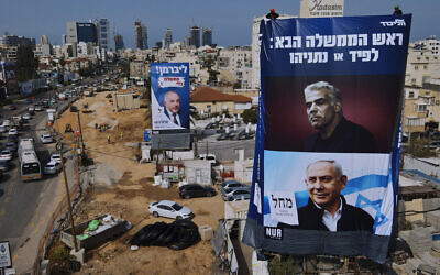 Workers hang an election campaign billboard for the Likud Party showing a portrait of its leader Prime Minister Benjamin Netanyahu, lower right, and opposition party leader Yair Lapid, upper right, next to a billboard of the Yisrael Beitenu Party showing its leader Avigdor Lieberman, in Bnei Brak, Sunday, March. 14, 2021. (AP Photo/Oded Balilty)