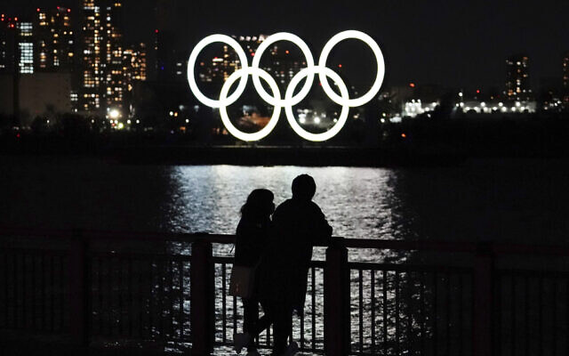 A man and a woman stand with the backdrop of the Olympic rings floating in the water in the Odaiba section in Tokyo, March 3, 2021. (AP Photo/Eugene Hoshiko)