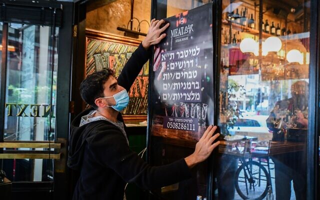Worker puts up a poster advertising for staff at a restaurant in Tel Aviv, on March 3, 2021 (Avshalom Sassoni/Flash90)