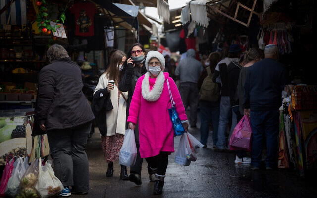 People wear protective face masks as they walk through the Carmel market in Tel Aviv, on March 4, 2021 (Miriam Alster/FLASH90)