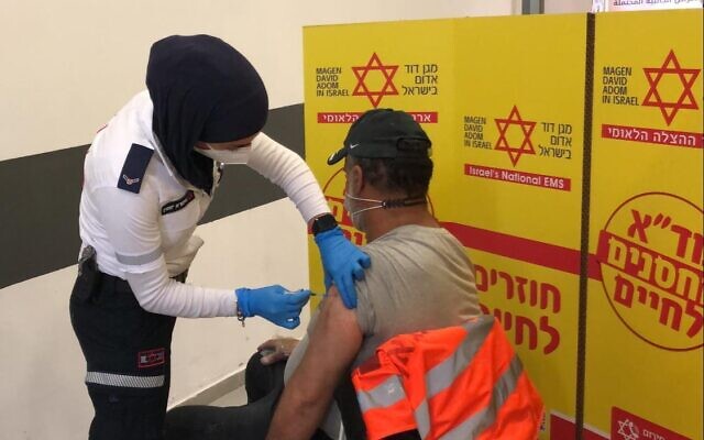 A Palestinian worker gets vaccinated by Israeli Magen David Adom staff at the Sha'ar Efraim checkpoint in the West Bank, March 4, 2021 (COGAT)