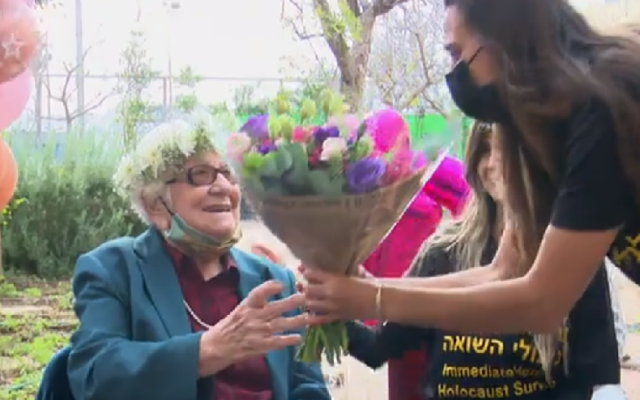 A volunteer from the Association for Immediate Help of Holocaust Survivors gives Frieda Kliger flowers for her 100th birthday on March 14th 2021. (Screen capture: Channel 12 News)