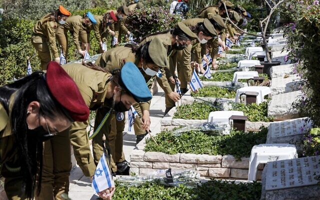 Soldiers place Israeli national flags showing black sashes atop with the Hebrew word "Remembrance" on graves, at the Kiryat Shaul military cemetery in the Mediterranean coastal city of Tel Aviv on April 13, 2021, as they pay respects to fallen soldiers on Yom HaZikaron (Memorial Day). (JACK GUEZ / AFP)