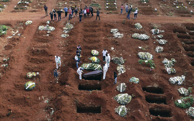 In this April 7, 2021, file photo, cemetery workers wearing protective gear lower the coffin of a person who died from complications related to COVID-19 into a gravesite at the Vila Formosa cemetery in Sao Paulo, Brazil. (AP/Andre Penner, File)