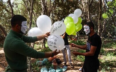 Masked Hamas members apparently prepare incendiary balloons to be launched toward Israel from the Gaza Strip, on May 8, 2021. (Mohammed Abed/AFP)