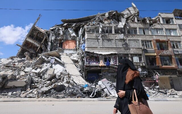 A Palestinian woman walks past a destroyed building in the al-Rimal commercial district in Gaza City on May 22, 2021, following a ceasefire between Israel and Palestinian terror groups. (Emmanuel Dunand/AFP)