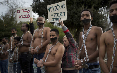 In this Wednesday, January 17, 2018 file photo, Eritrean migrants wear chains to mimic slaves at a demonstration against the Israeli government's plan to forcibly deport African refugees and asylum seekers from Israel to Uganda and Rwanda, outside the Knesset in Jerusalem. (AP/Oded Balilty)