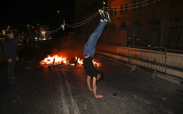 A Palestinian protester does a handstand next to a fire which was set on a road during clashes with Israeli police near Damascus Gate just outside Jerusalem’s Old City on May 9, 2021. (AP Photo/Ariel Schalit)