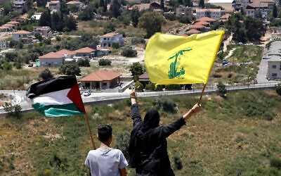 In this May 15, 2021, file photo, Lebanese wave Hezbollah and Palestinian flags, as they stand in front of the Israeli town of Metula, background, on the Lebanese side of the Lebanese-Israeli border in the southern village of Kfar Kila, Lebanon. (AP Photo/Hussein Malla, File)