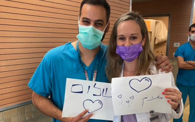 Illustrative image: Medical workers, one Jewish and one Arab, holding signs calling for peace, at Rambam Medical Center, May 2021 (courtesy of Rambam Medical Center)