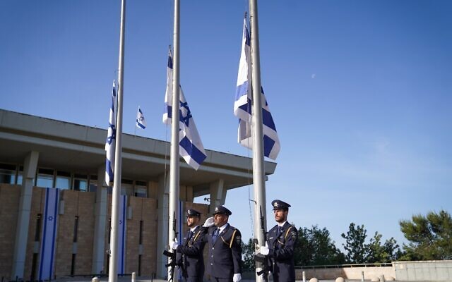 The Knesset Guard lowers Israeli flags to half-staff outside the Knesset in Jerusalem as a national day of mourning begins for victims of the Meron disaster, May 2, 2021. (Noam Moskowitz/Knesset)