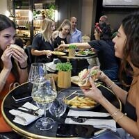 Diners eat burgers made with "cultured chicken" meat at a restaurant adjacent to the SuperMeat production site in the central Israeli town of Ness Ziona on June 18, 2021 (JACK GUEZ / AFP)